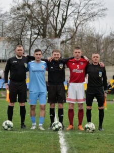 Football players and referees posing together before a match on an outdoor field.